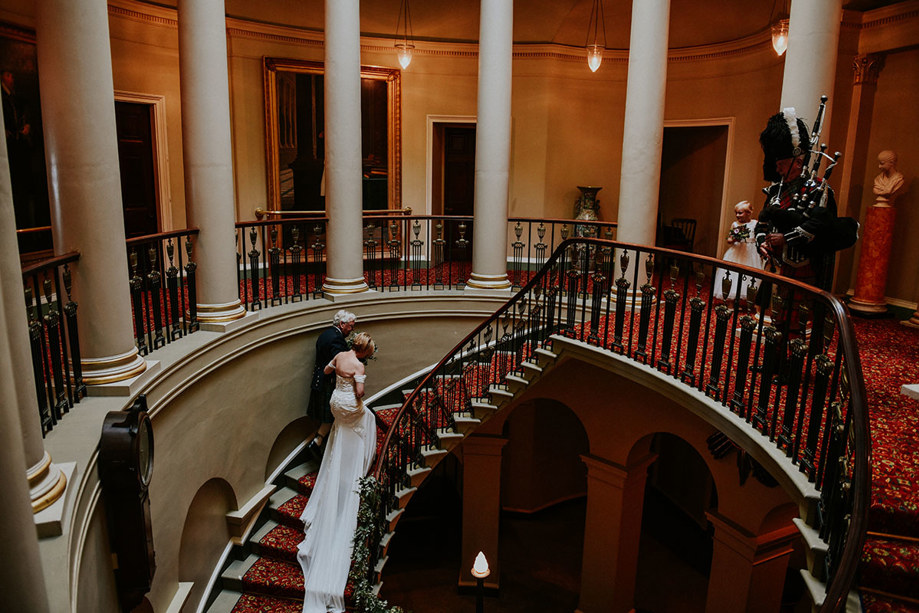 Newlyweds walk up the grand Oval Staircase with moody lighting and columns